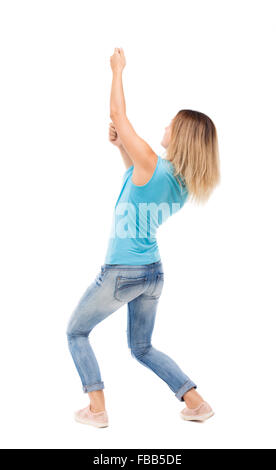 back view of standing girl pulling a rope from the top or cling to something. girl watching. Rear view people collection. backside view of person. Isolated over white background. blonde in a blue shirt and jeans, pulls the top of the rope. Stock Photo