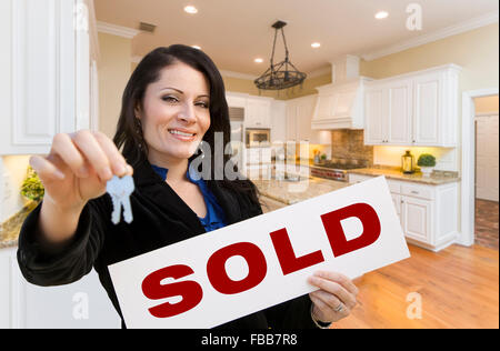 Pretty Hispanic Woman In Kitchen Holding House Keys and Sold Sign. Stock Photo