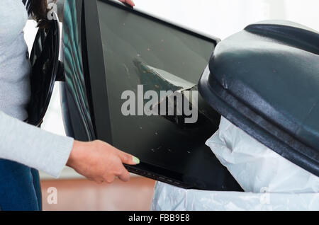 Broken computer screen going into large black trash dumpster. Stock Photo