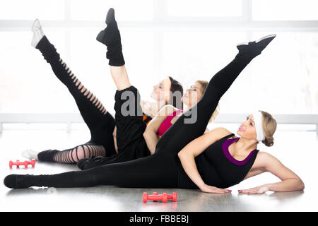 Fitness practice, group of three sporty females stretching, doing leg swings, exercises for flexibility, problem zones, hips, wa Stock Photo