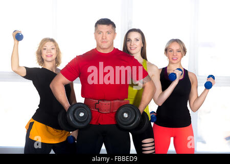 Muscular bodybuilder and three athletic women holding dumbbells. Group of four sporty people posing with freeweights in class. A Stock Photo