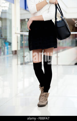 Female model in cute trendy outfit for shopping, office or study. Close-up on legs. Young shopper woman walking in short black s Stock Photo