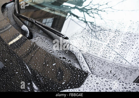 Black car hood fragment and windshield wipers with raindrops on it, closeup photo with selective focus and shallow DOF Stock Photo