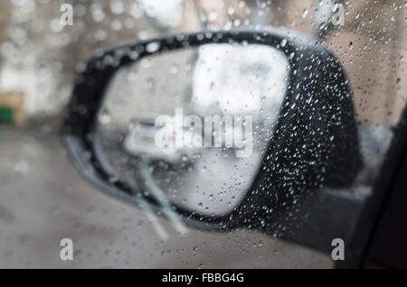 Wet car window with raindrops and mirror behind. Close-up photo with selective focus and shallow DOF Stock Photo