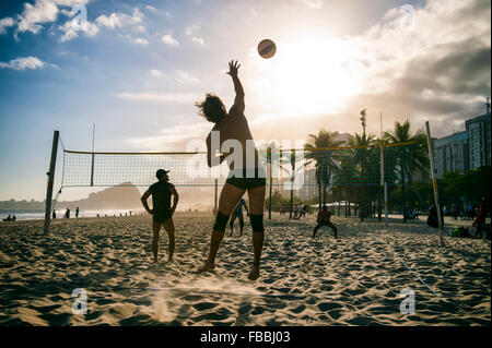 RIO DE JANEIRO, BRAZIL - OCTOBER 30, 2015: A group of young Brazilian men play game of volleyball at sunset on Copacabana Beach. Stock Photo