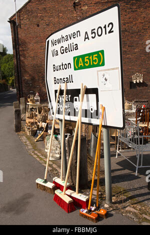 UK, England, Derbyshire, Cromford, Market Square Antiques and Hardware shop brushes for sale leaning against road sign Stock Photo