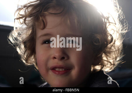 Landscape portrait of curly haired Caucasian toddler boy with sunlight shining through his hair from behind Stock Photo