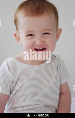Portrait of a cute red haired Caucasian baby girl wearing a striped white vest Stock Photo