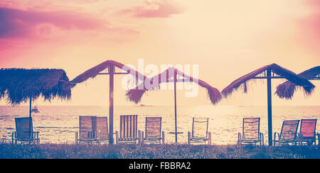 Vintage toned beach chairs and umbrellas at sunset, holidays background. Stock Photo
