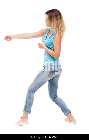 back view of standing girl pulling a rope from the top or cling to something. girl watching. Rear view people collection. backside view of person. Isolated over white background. The girl in jeans and a blue shirt pulling the rope. Stock Photo