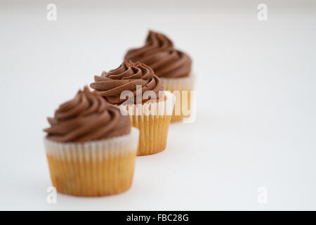 A row of three chocolate cupcakes on an isolated white background.  Middle cupcake in focus, front and back cupcakes out of focu Stock Photo