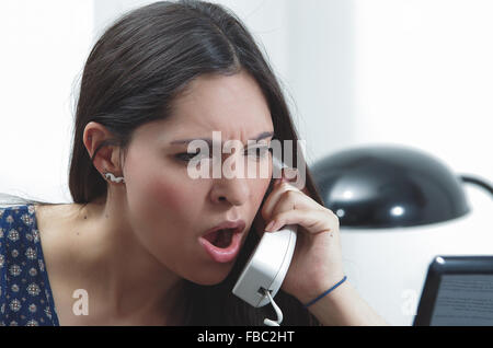 Hispanic brunette sitting by office desk talking on telephone with occupied and worried facial expression Stock Photo