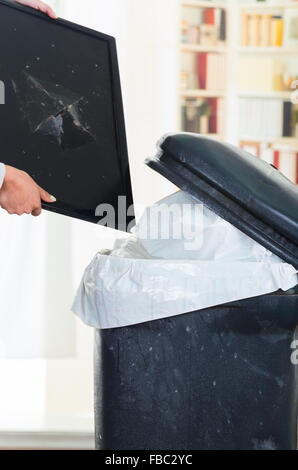 Broken computer screen going into large black trash dumpster Stock Photo