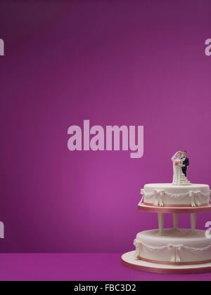 Wedding cake with husband and wife topper against colored background Stock Photo