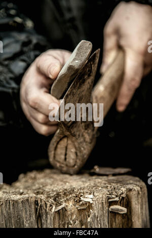 Close-up of male hands sharpening dirty old rusty axe with a grindstone on tree stump Stock Photo
