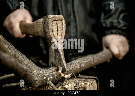 Close-up of male hands chopping firewood, tree branch on stump with old rusty axe Stock Photo