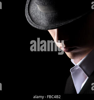 Handsome unrecognizable man in hat, his face in the shadows, minimalistic studio shot against black background, low key lighting Stock Photo