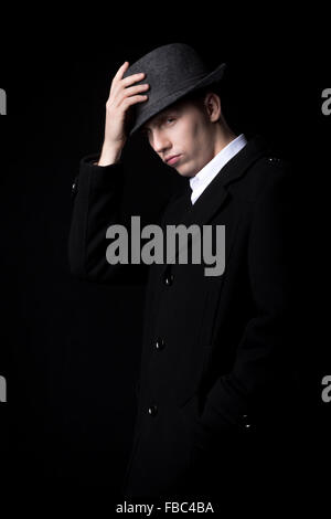 Brutal looking male person in the darkness, touching his hat, greeting with wicked, shrewd expression, low key studio shot Stock Photo