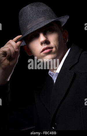 Brutal looking man hiding his eyes in the darkness, touching his hat, greeting, unrecognizable person, low key studio shot Stock Photo