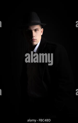 Good-looking guy in hat and coat with confident serious look, fashionable and handsome, low key studio shot against black backgr Stock Photo
