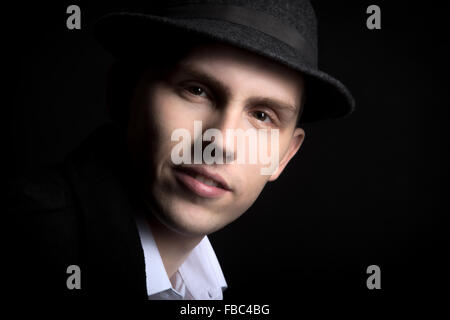 Portrait of smiling attractive young male model in hat with confident look, studio shot against black background Stock Photo