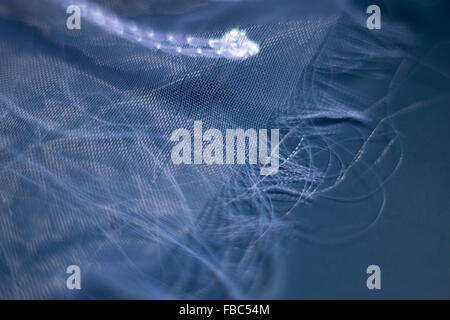 Unraveling edge of transparent white fabric on blue background Stock Photo