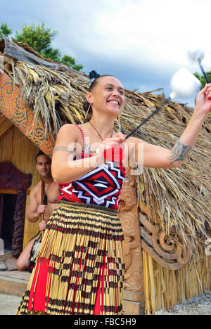 Maori woman and Maori man in Te Puia Maori Village Rotorua. Woman is dancing with Poi(s) while the man is in the hut behind. North Island, New Zealand Stock Photo