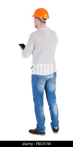 young engineer in a protective helmet with tablet computer in the hands of. Rear view people collection. backside view of person. Isolated over white background. Engineer verifies the work done with the list in the plate. Stock Photo