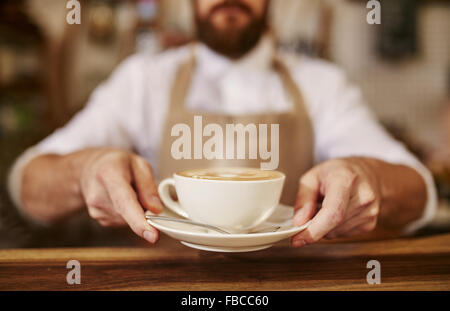 Close up of male barista serving cup of fresh coffee. Cup of coffee in the hands of waiter.