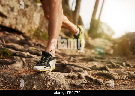 Close-up of trail running shoe on challenging rocky terrain. Male runner's legs working out on extreme terrain outdoors. Stock Photo