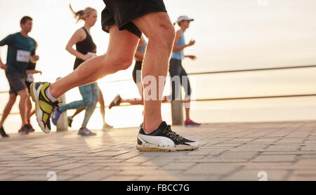 Closeup portrait of people running on road by the sea with focus on feet of male runner. Stock Photo