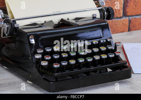 Vintage typewriter, notepad, pencil and china tea cup with tea on old shabby wood effect desk  top with red brick wall backgroun Stock Photo