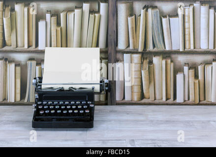Vintage typewriter on old shabby wood effect desktop with old bookcase background Stock Photo