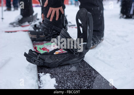 Person preparing to go snowboarding tightening the straps on his snowboard in winter snow at a resort Stock Photo