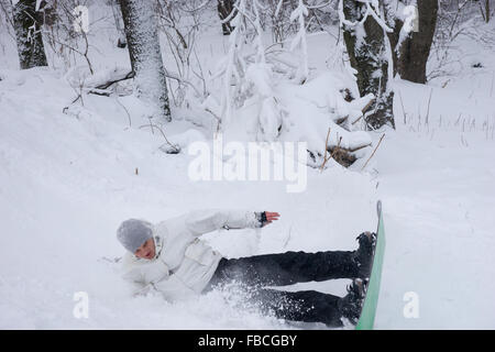 Young man practicing a jump on his snowboard landing on his side in the snow in a flurry of snowflakes Stock Photo