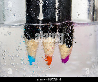 Watercolour pencils in a clear tumbler or glass half full of sparkling water showing bubbles on a white background. Stock Photo