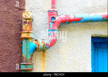 A rusted metal drainpipe with peeling blue and red paint Stock Photo