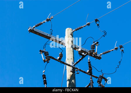 Old wooden telephone or electrical pole and metal bar with cables and insulators on right side, against clear blue sky. Stock Photo