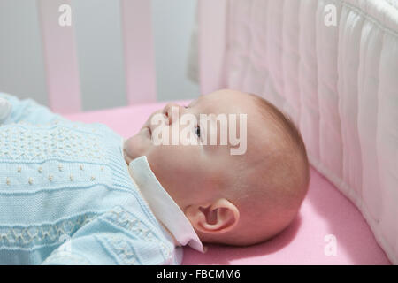 Awake four month baby boy lying in cot with bumper pad. Side view Stock Photo