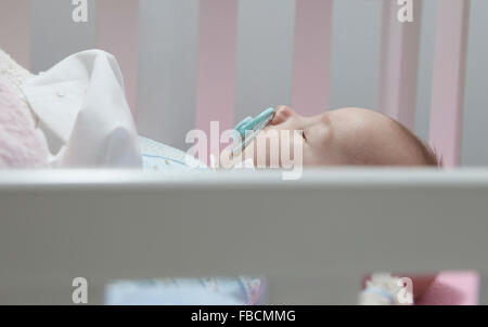 Sleeping four month baby boy lying in cot with pacifier. Side view Stock Photo