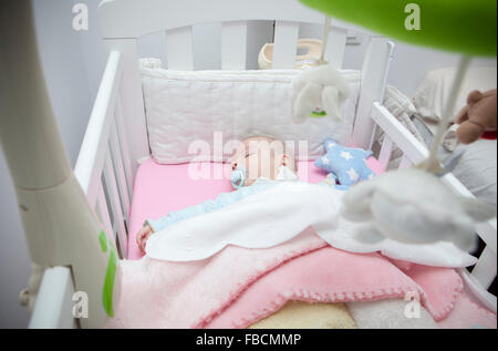 Sleeping four month baby boy lying in cot with mobile. Overhead view Stock Photo