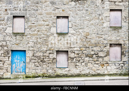 Part of the exterior of an old stone house in Scotland with boarded up windows a blue wooden door Stock Photo
