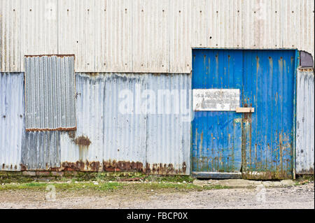 Rusted metal sheets and a blue wooden door on the exterior of an old warehouse Stock Photo
