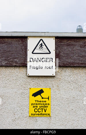 Warning signs on a building for a fragile roof and CCTV surveillance Stock Photo