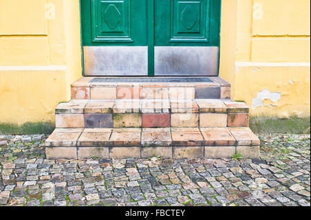 Tiles steps outside a yellow urban building with a green door Stock Photo