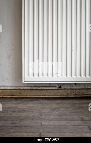 Part of a radiator against a wall over a wooden floor Stock Photo