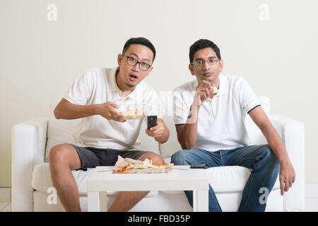 Group of friends sitting on sofa watching football match together at home. Stock Photo