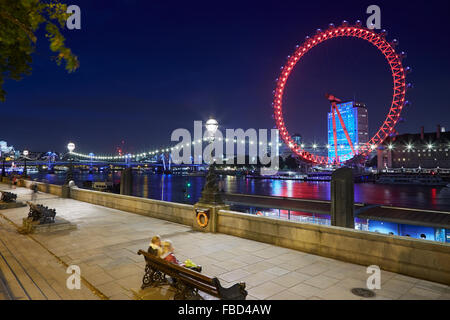 London eye, ferris wheel, illuminated in red in the night and Thames river docks view Stock Photo