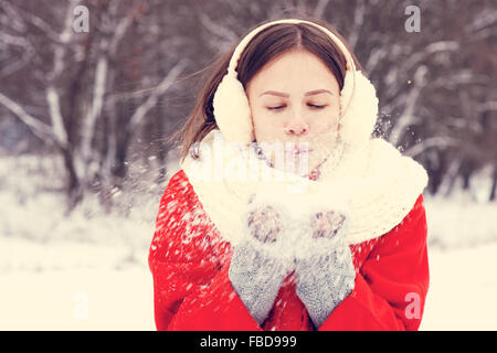 Beauty Winter Girl Blowing Snow in frosty winter Park. Outdoors. Flying Snowflakes. Sunny day. Backlit. Joyful Beauty young woma Stock Photo