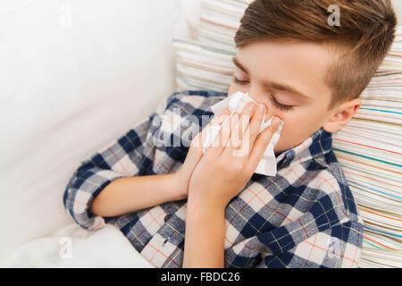 ill boy lying in bed and blowing his nose at home Stock Photo